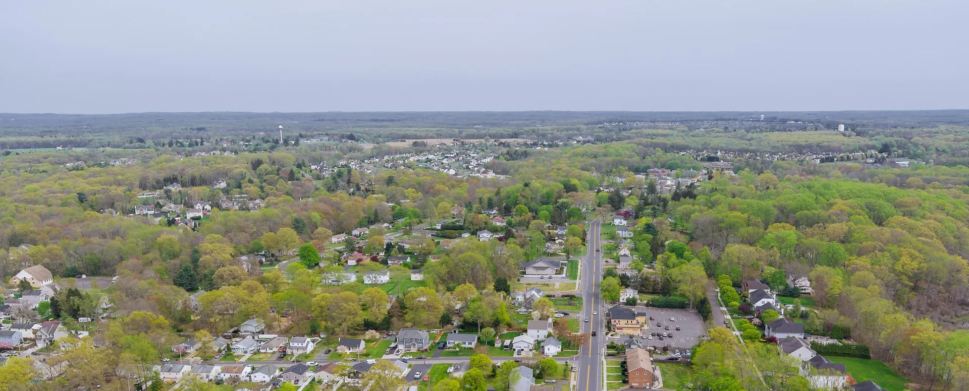An aerial view over a residential town, with houses and tree-lined streets along a main road
