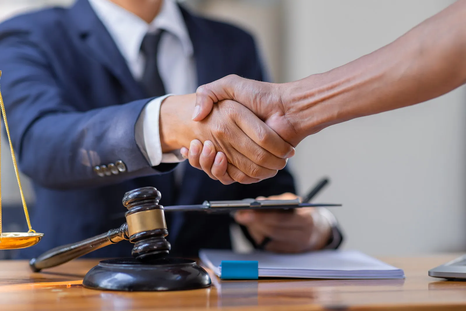 Two people shaking hands across a desk with a gavel and documents