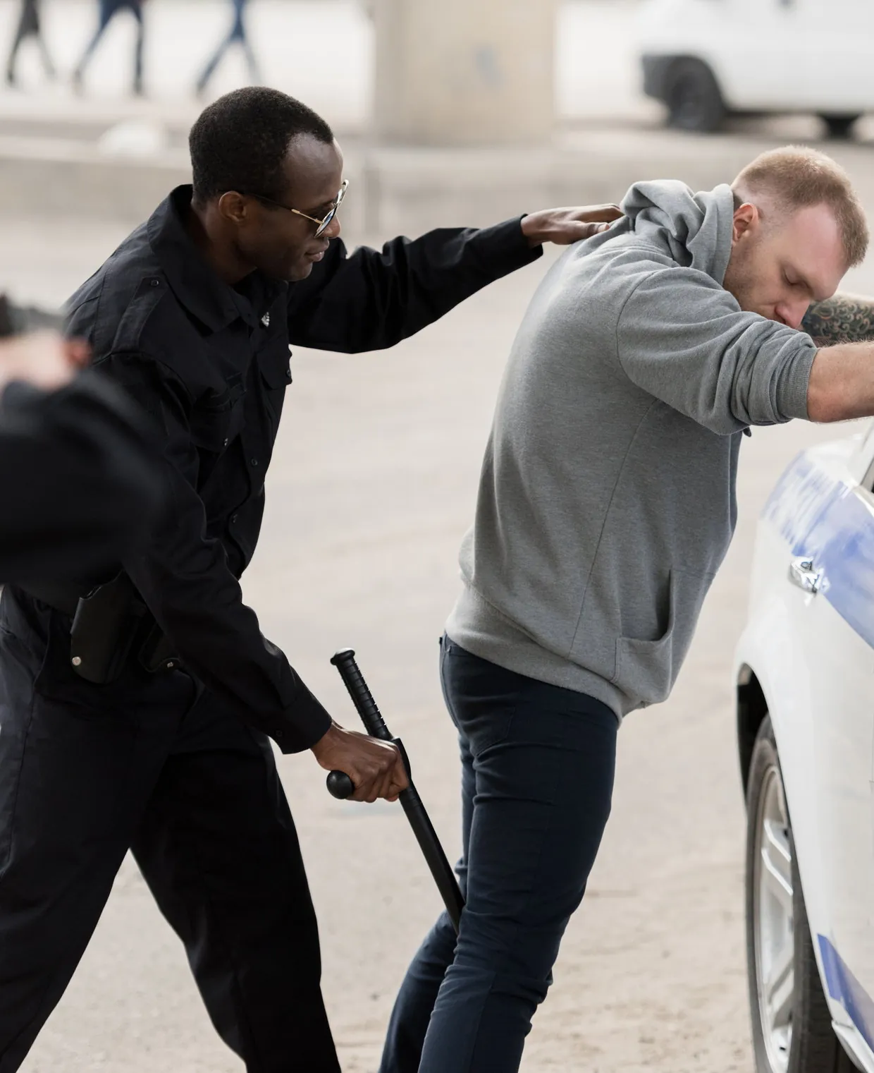 An officer with a baton beside a second officer making an arrest